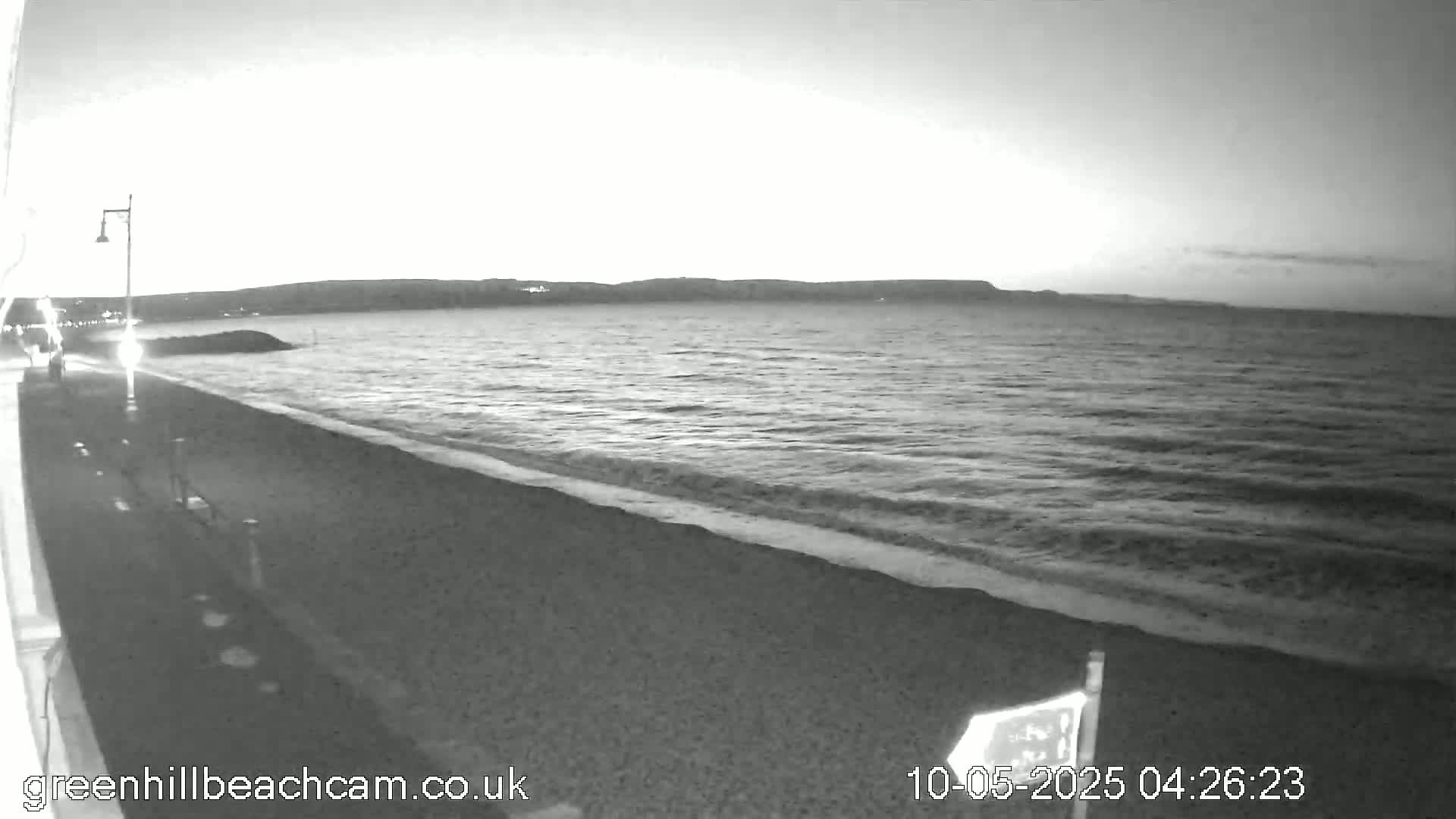 A dark beach with gentle waves lapping the shore under a twilight sky.