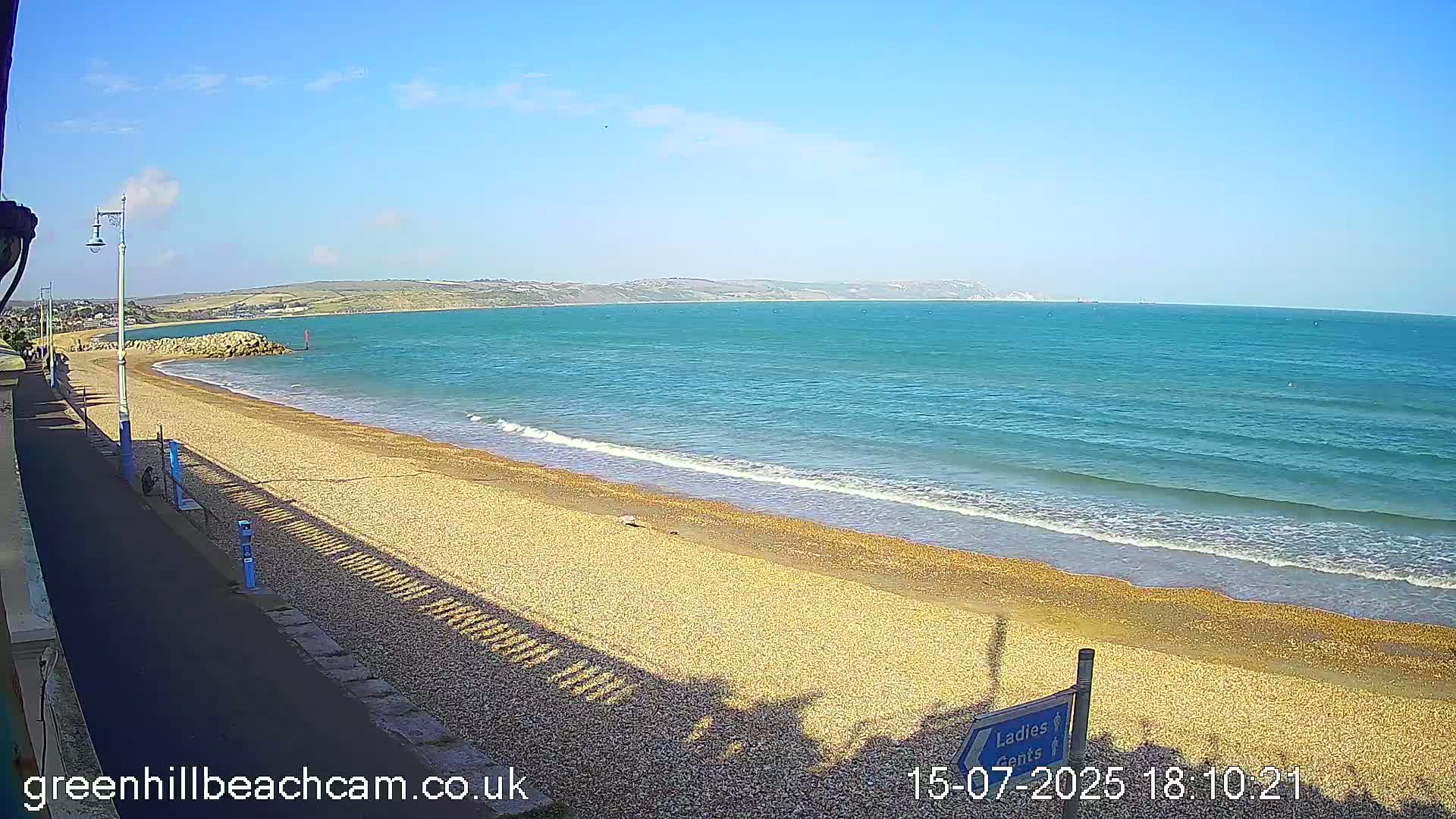A pebble beach with gentle waves laps the shore under a clear blue sky.