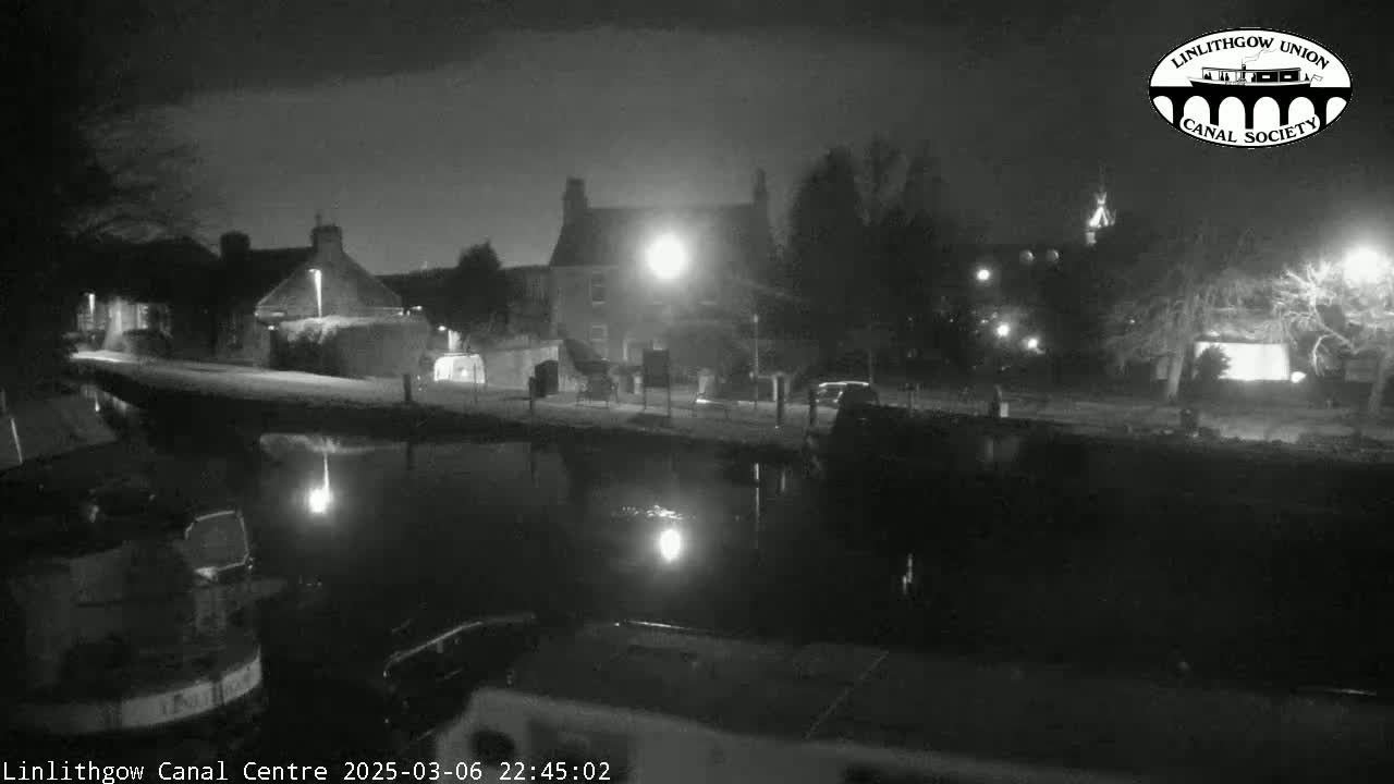 A nighttime, black-and-white view of a canal reflecting lights from buildings and street lamps on its banks.