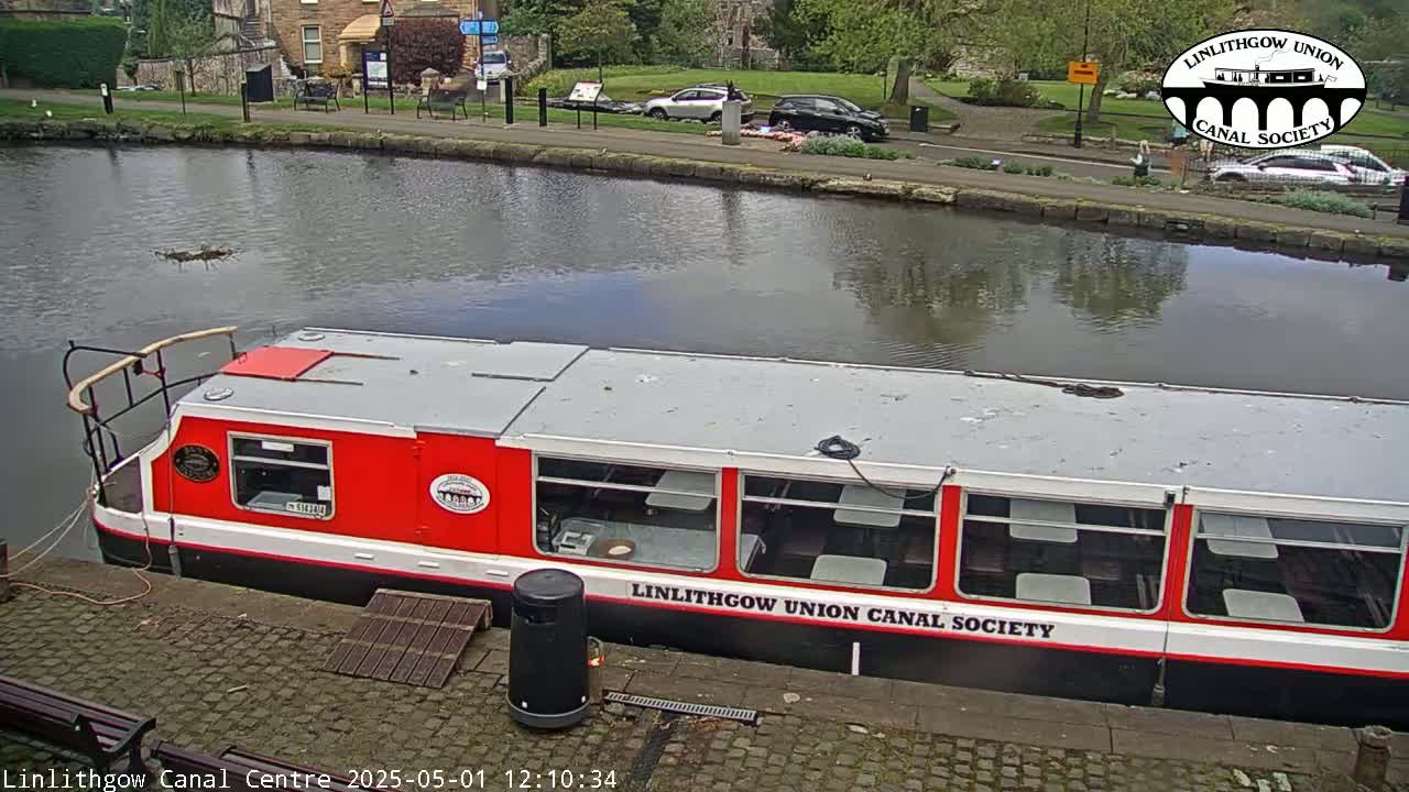 A red and white canal boat is docked at a canal side, under a partly cloudy sky.