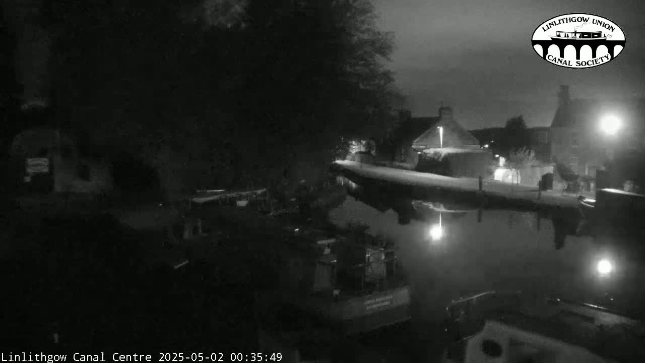 A nighttime, snow-covered canal scene shows buildings lining the waterway, with boats moored alongside.