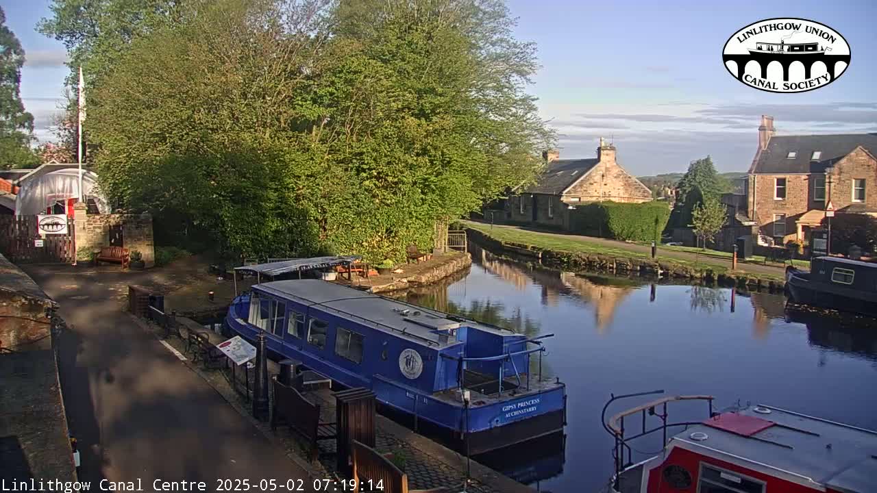 A blue canal boat is moored near a canal side building on a sunny day.