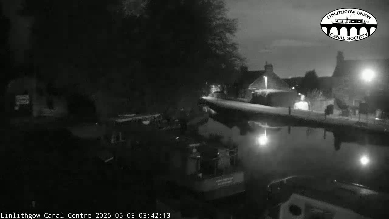 A nighttime, low-light view of a canal reflecting the dimly lit buildings and trees along its banks.