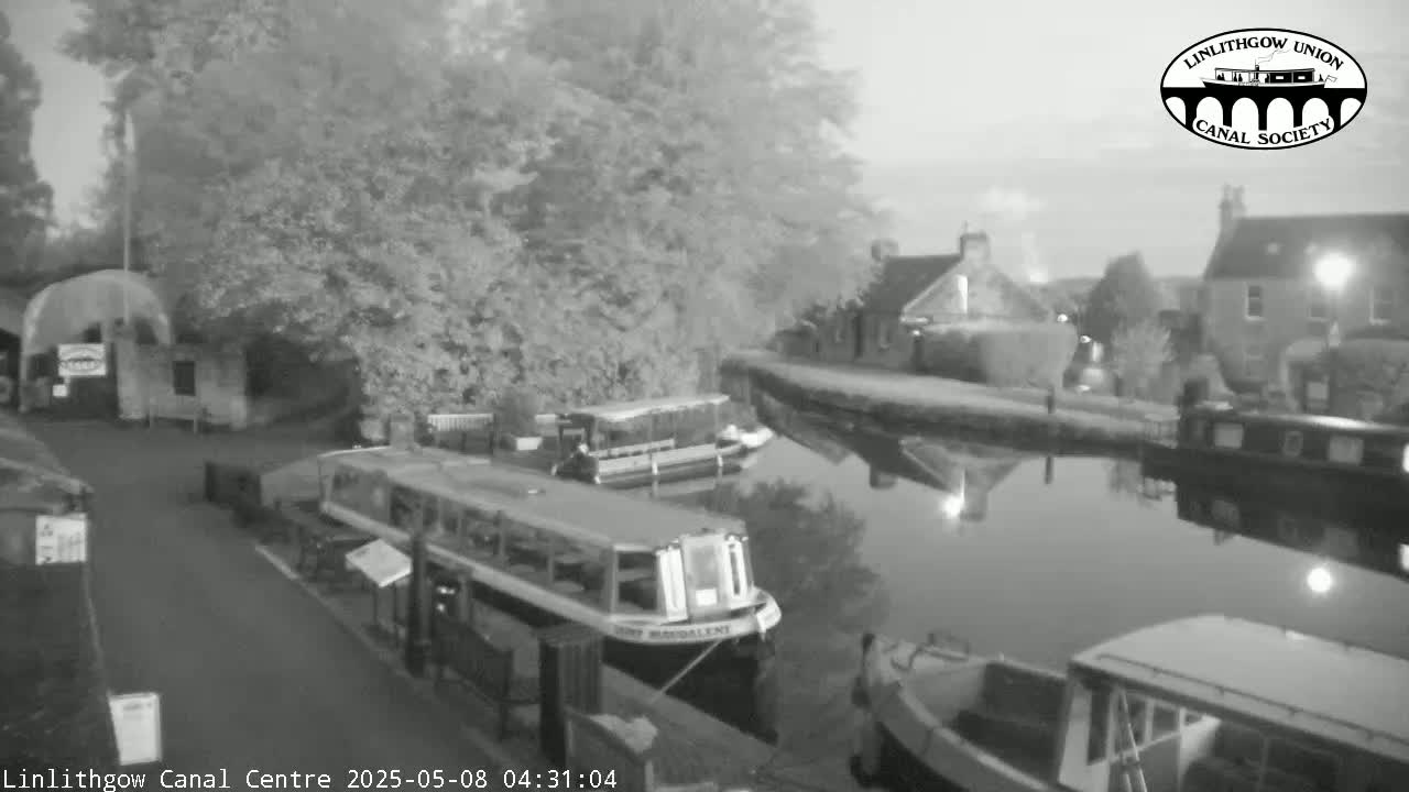A canal scene at dawn shows several boats moored alongside a waterway, with buildings and trees lining the banks.