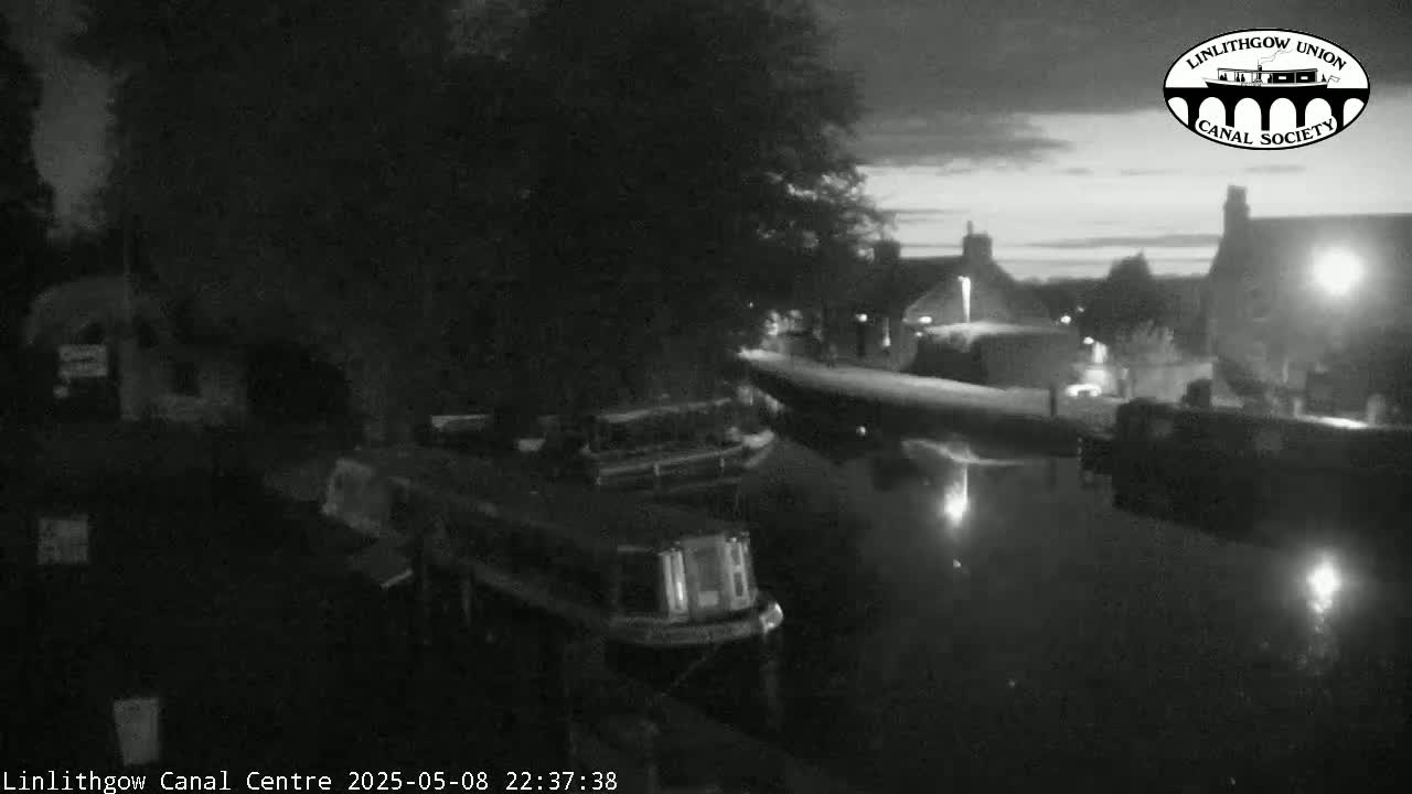 At night, several boats are moored along a calm canal, under a dark sky with a hint of twilight.