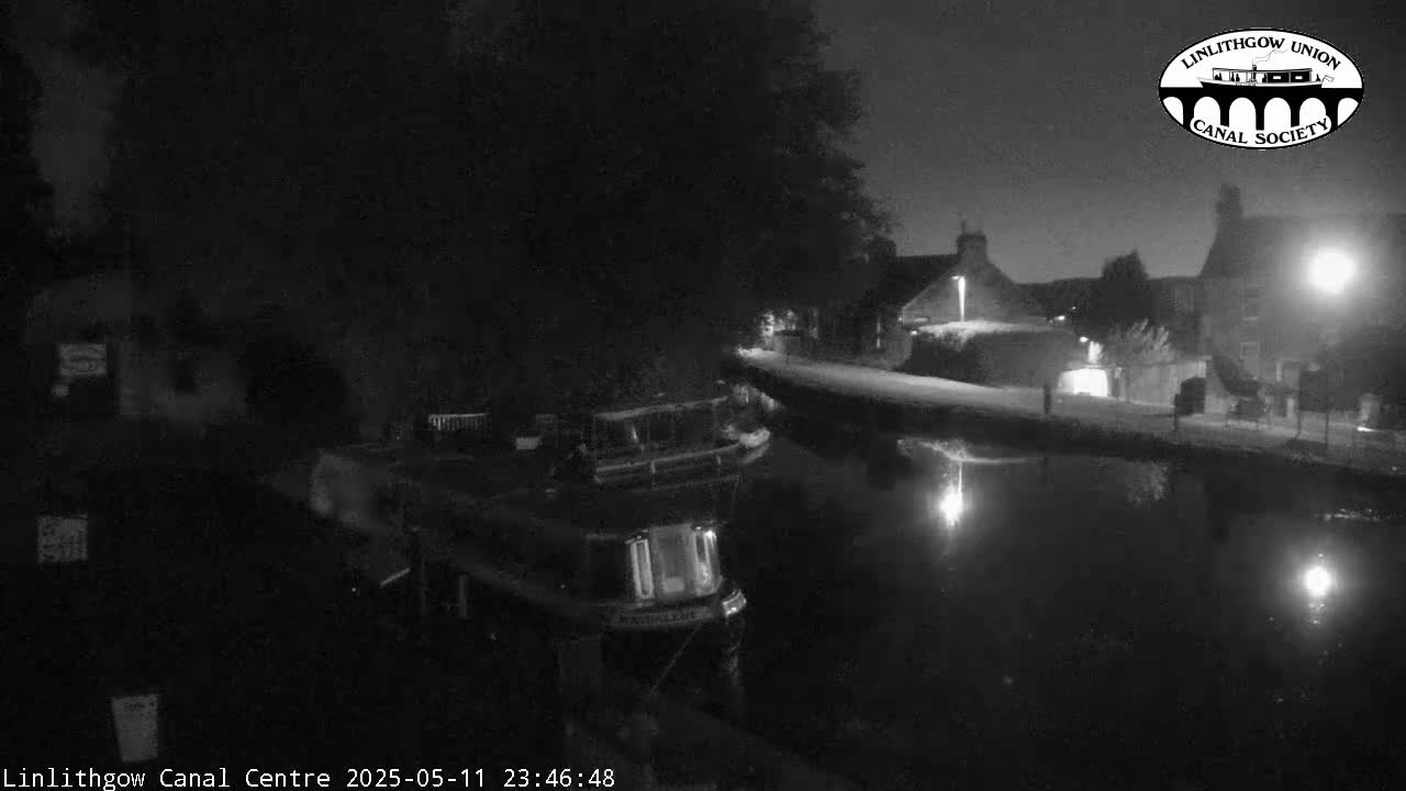 A narrowboat is moored on a canal at night under a dark sky.