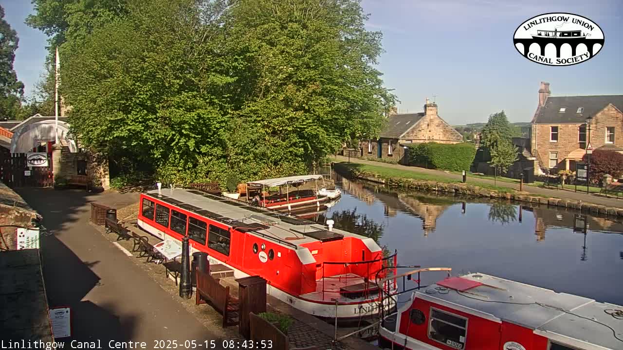 Two red canal boats are docked near a canal-side building on a sunny day.