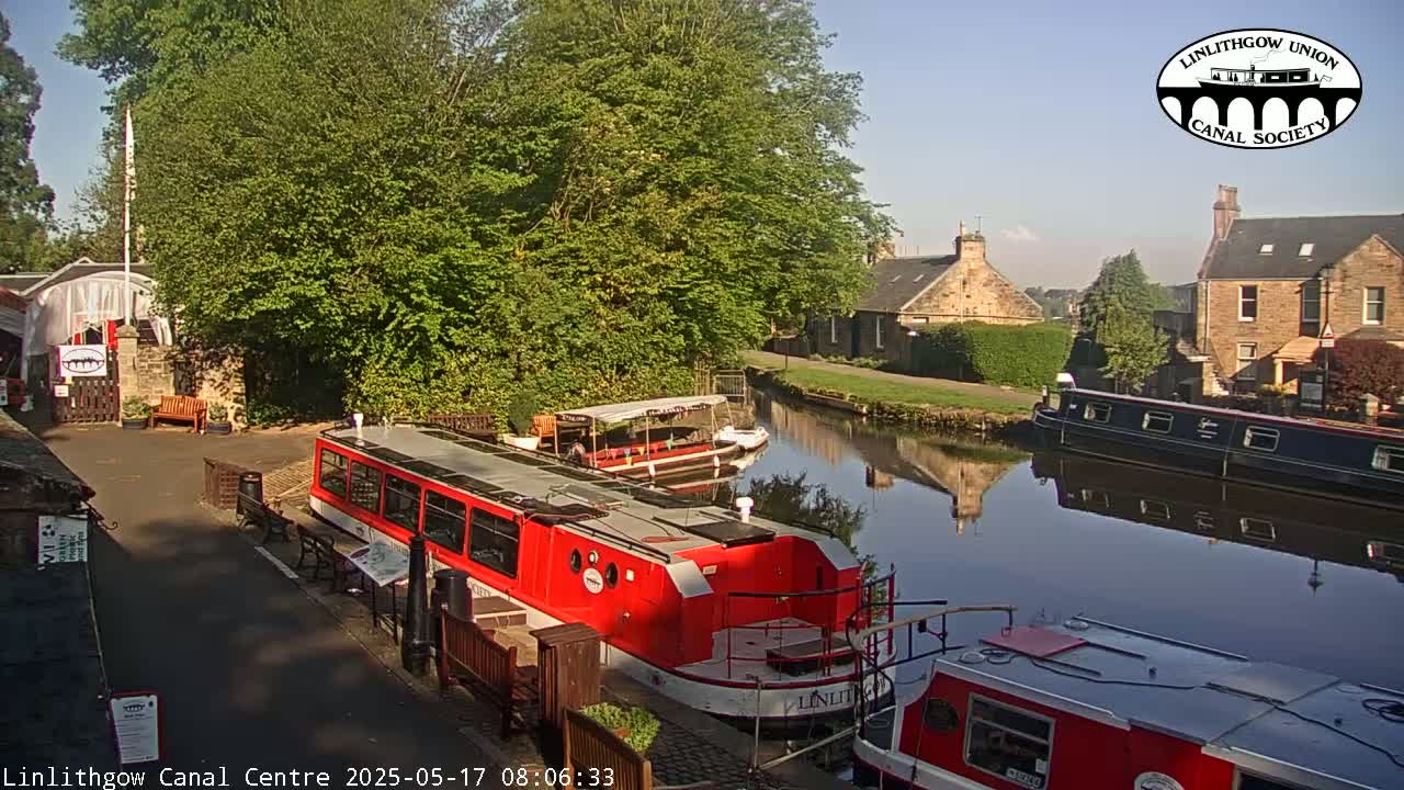 A sunny day at a canal, with several boats moored alongside a canal-side building and path.