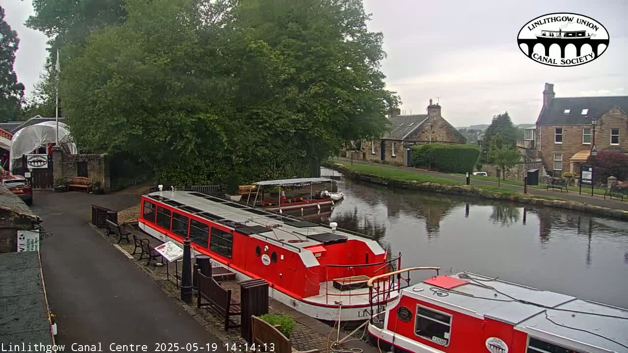 Two red canal boats are docked near a canal-side building under an overcast sky.