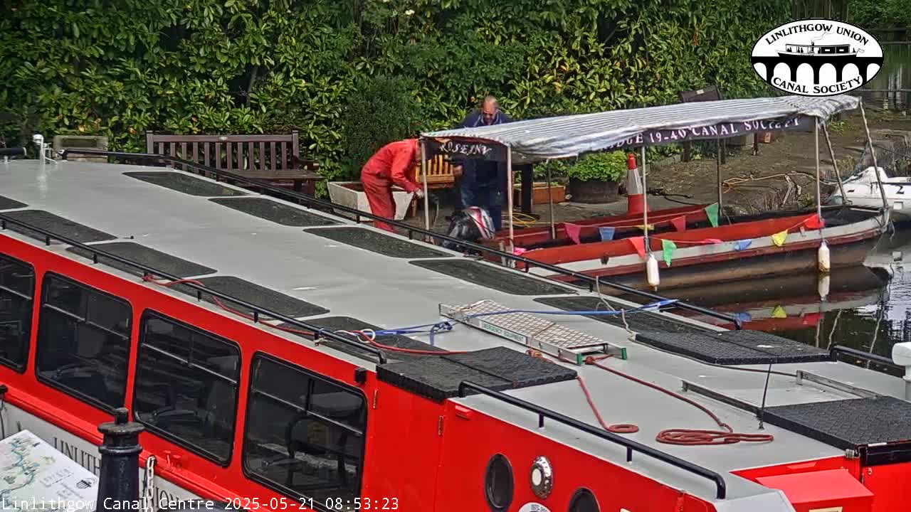 Two people are working near a red canal boat on an overcast day.
