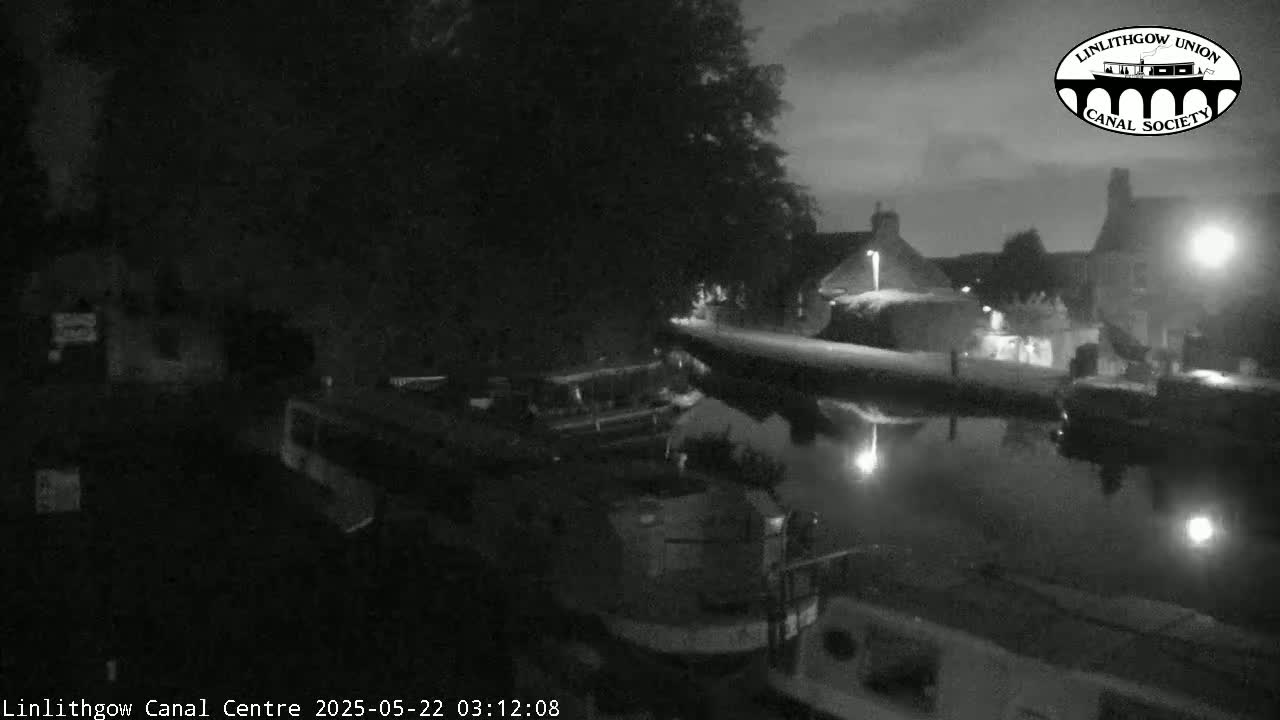 Several boats are moored along a dark canal at night under a cloudy sky.