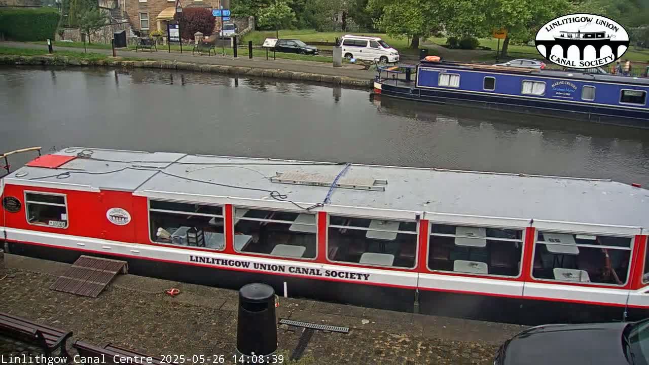 Two canal boats are moored on a calm canal, under an overcast sky.