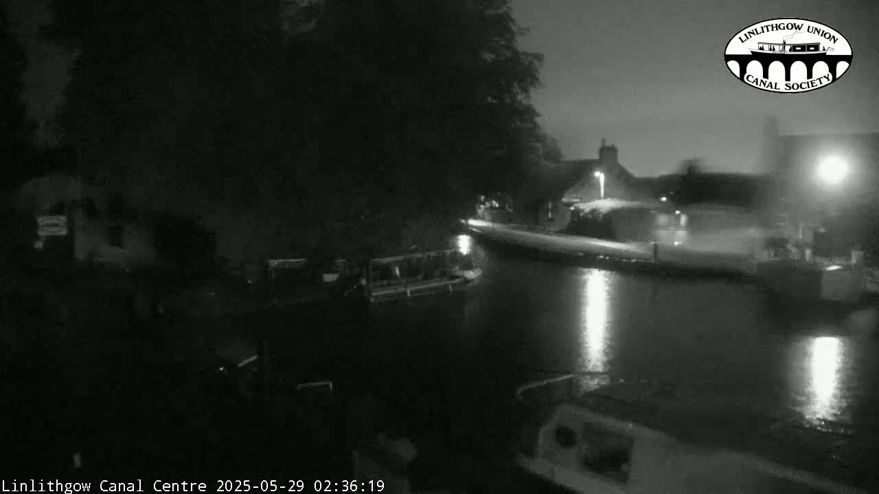 A nighttime view of a canal, showing boats moored along the water's edge under a dark sky.