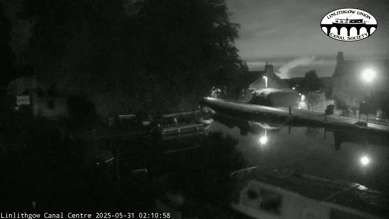 A nighttime, low-light view of a canal, with buildings and trees lining the banks, under a mostly clear sky.