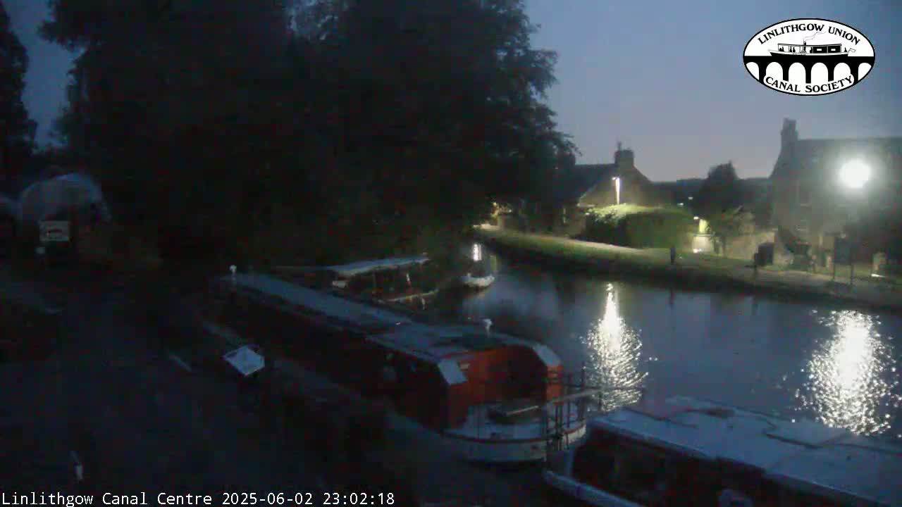 Several boats are moored along a canal at night under a dark, clear sky.