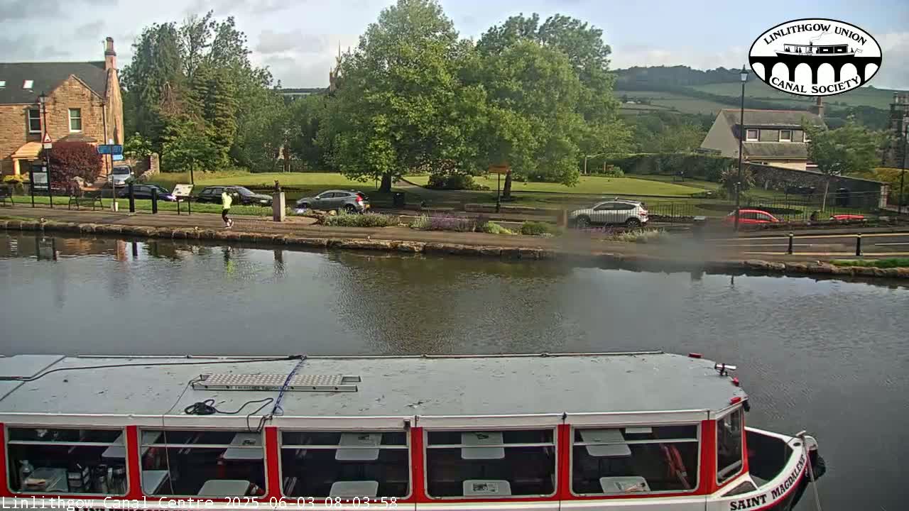 A canal scene on a partly sunny day shows a red and white canal boat in the foreground, with a person jogging along the canal path and several cars parked nearby.