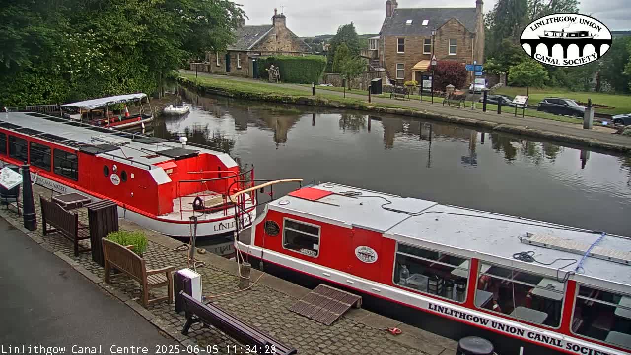 Two red and white canal boats are moored alongside a canal, under an overcast sky.