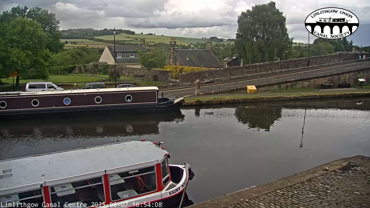 A canal scene under a cloudy sky shows two boats on the water near a stone bridge and buildings in the background.