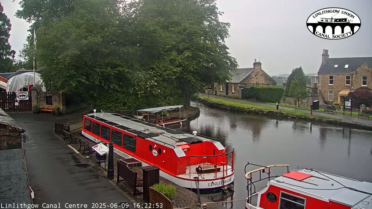 A red canal boat is docked near a stone building beside a calm canal on an overcast day.