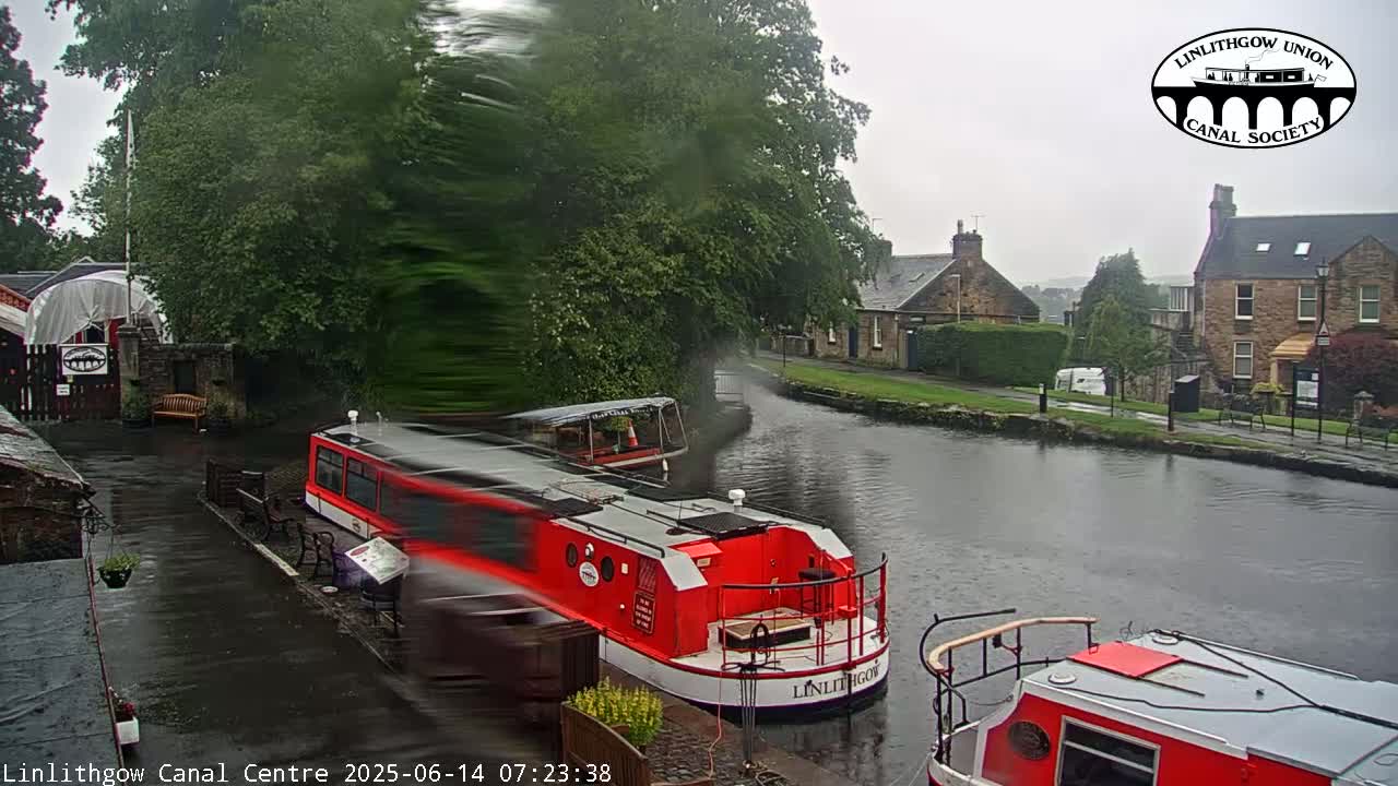 A red canal boat is docked near a calm canal reflecting a twilight sky, with buildings and trees lining the waterway.