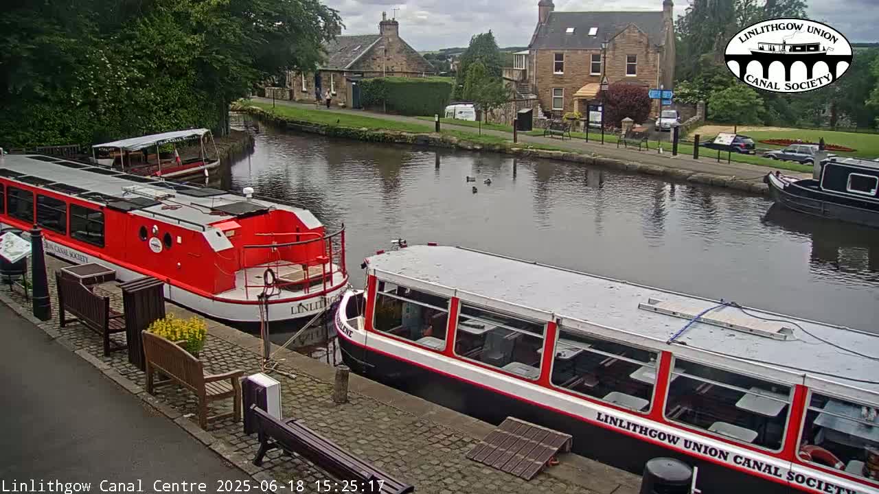 Two canal boats are docked near a stone building and a calm canal under an overcast sky.