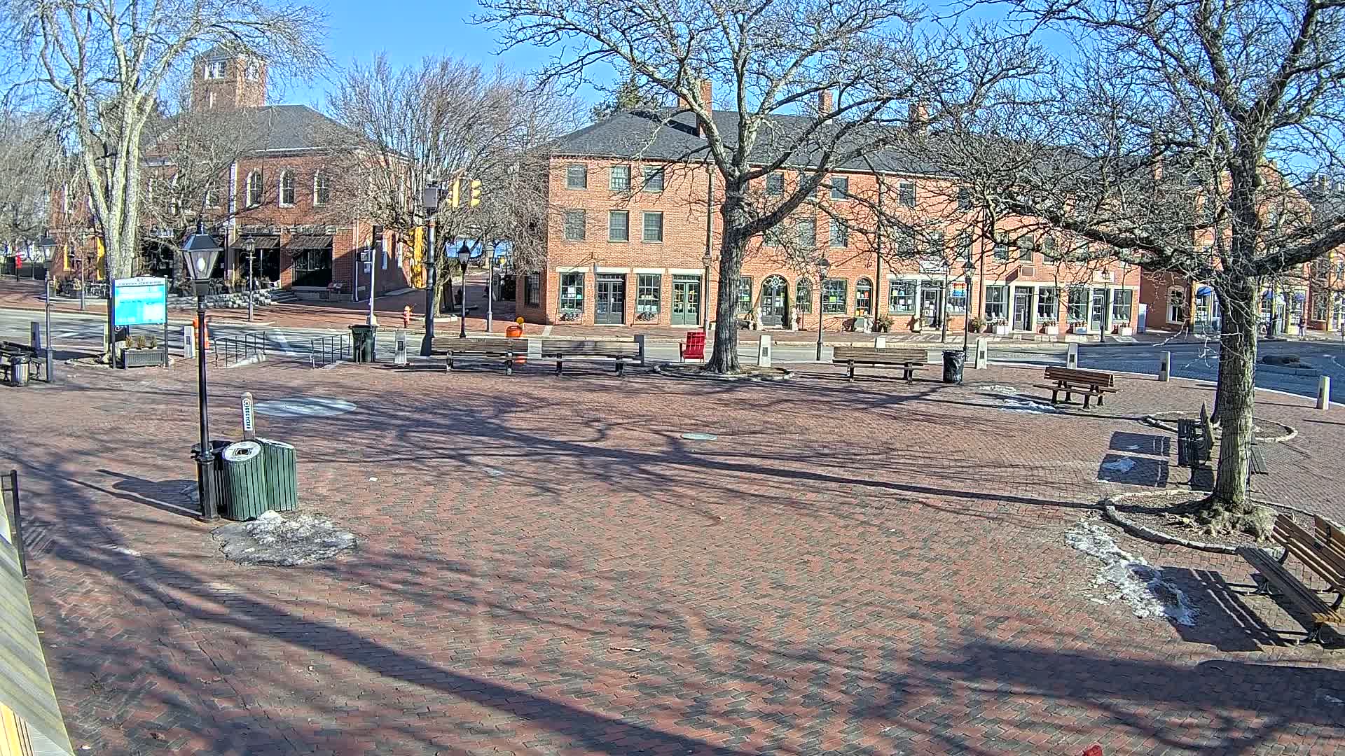 A brick town square with benches and trees under a sunny winter sky.