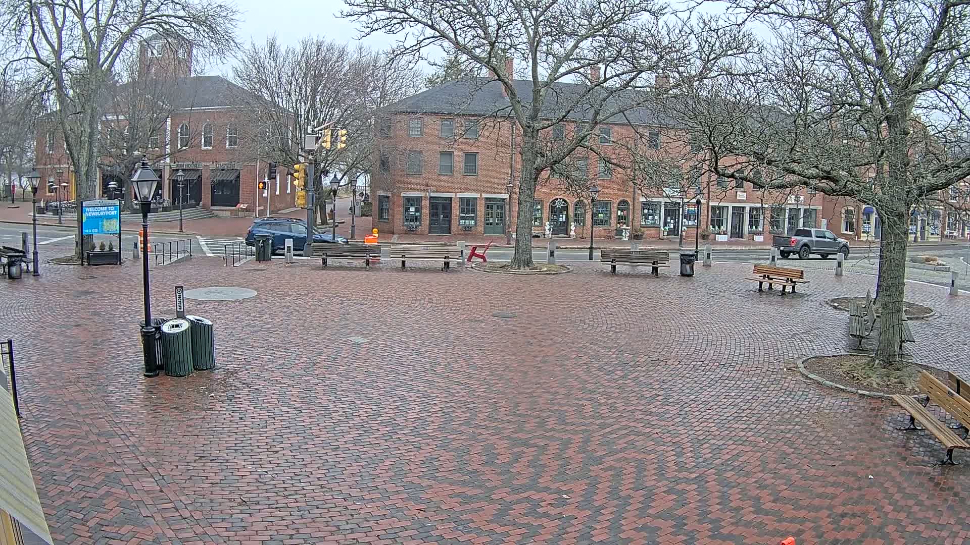 A brick town square with several benches and bare trees under an overcast sky.