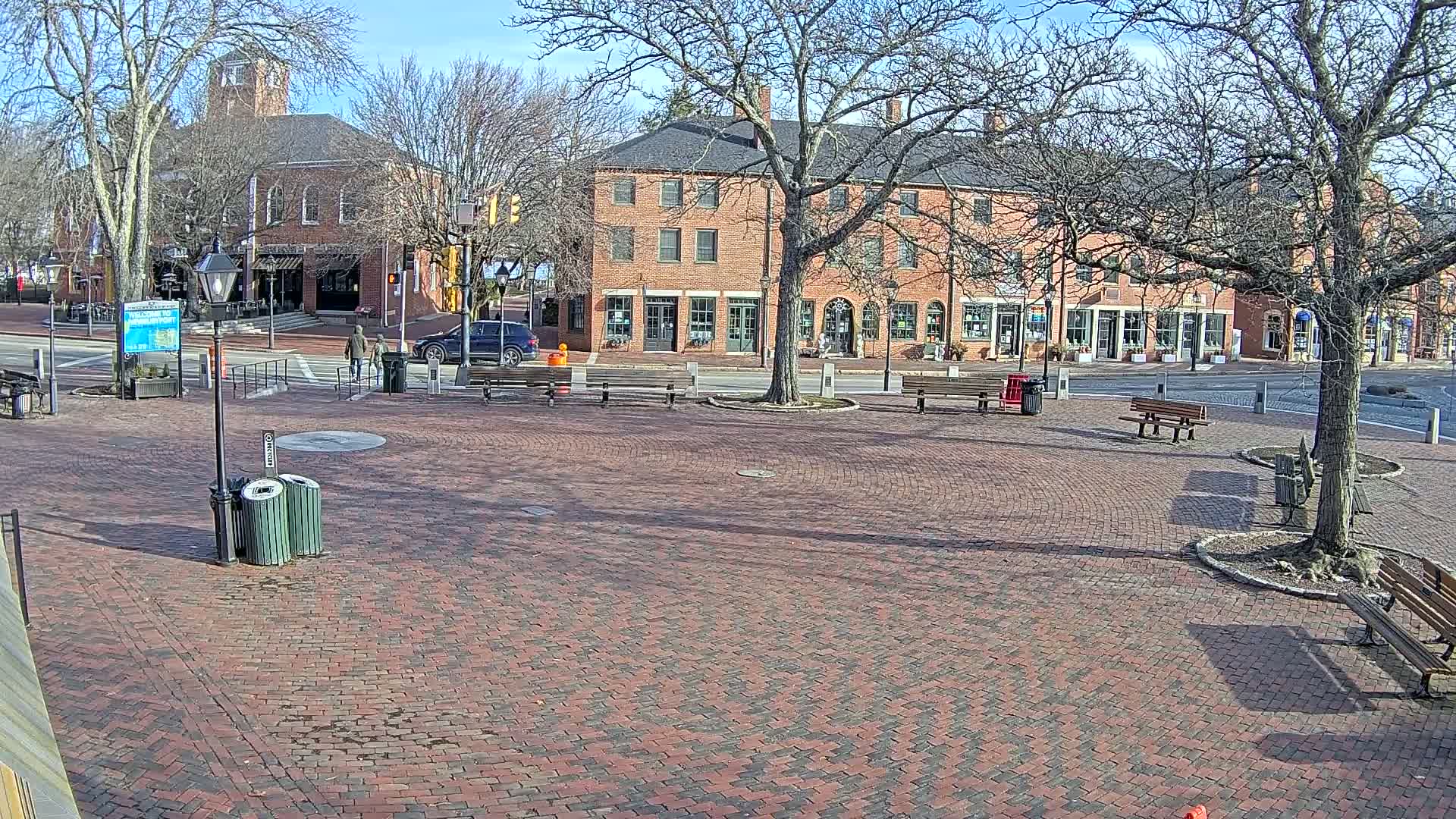 A brick plaza with benches and trees sits in front of several brick buildings on a sunny day.
