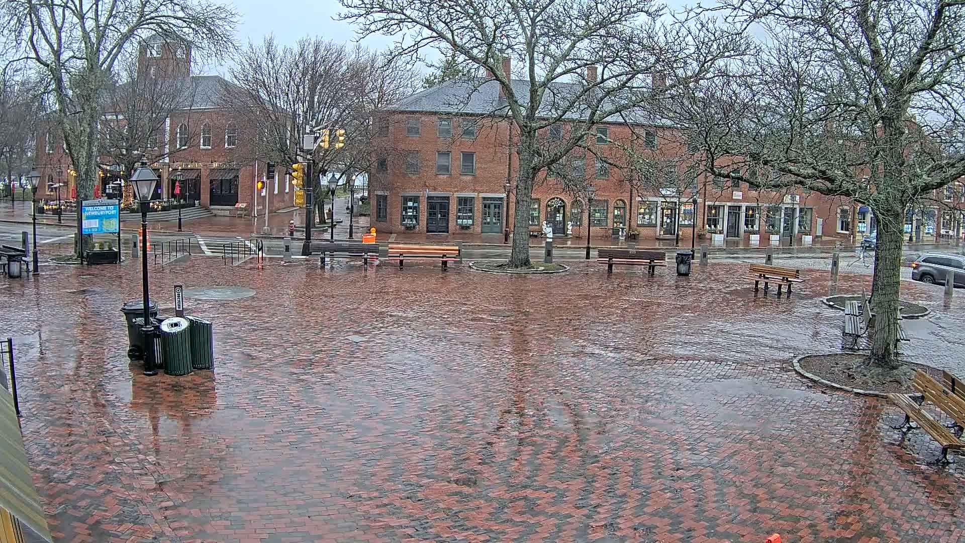 A wet brick town square with benches and brick buildings under a gray, overcast sky.