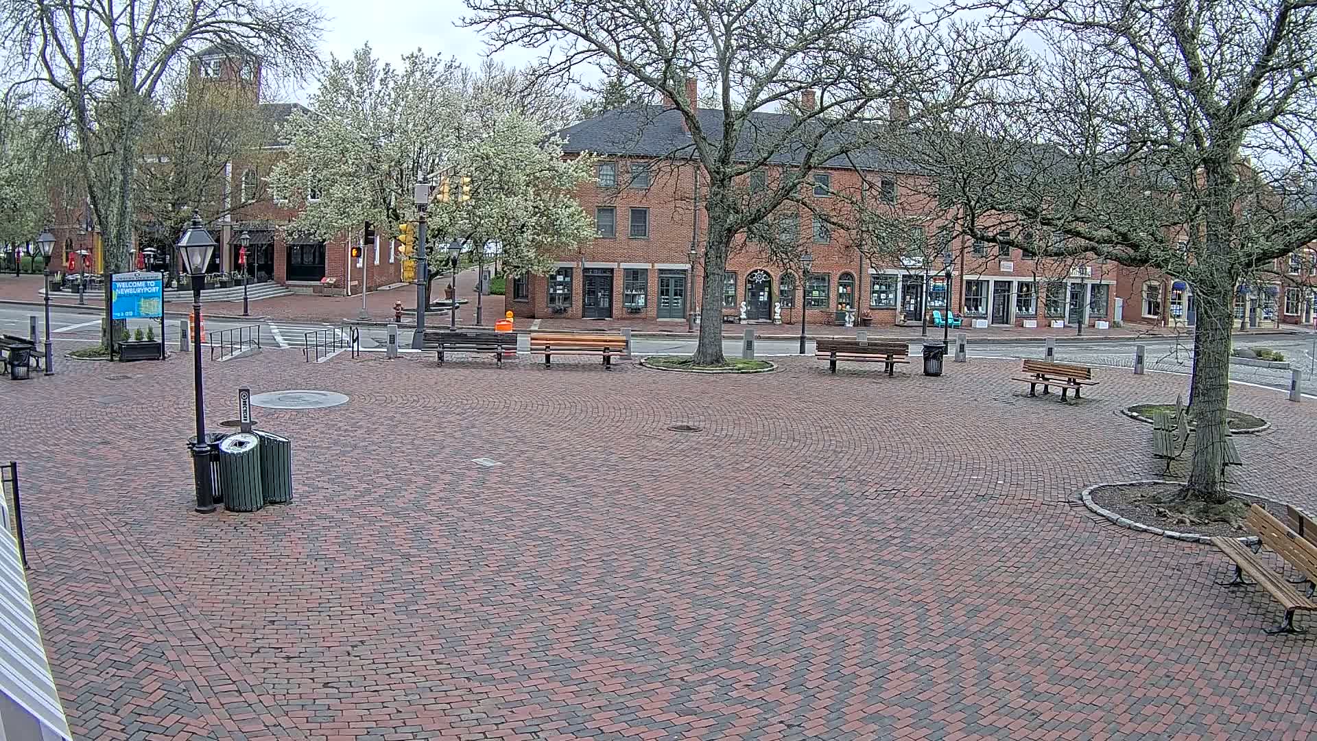 A brick plaza with several benches sits in front of a row of brick buildings under a cloudy sky.