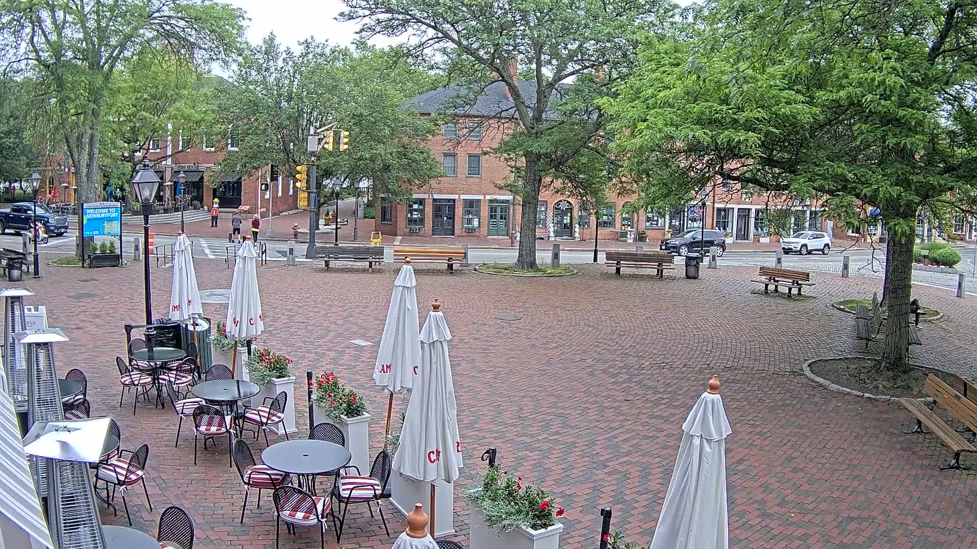 A brick plaza with outdoor café seating, surrounded by trees and brick buildings, on an overcast day.