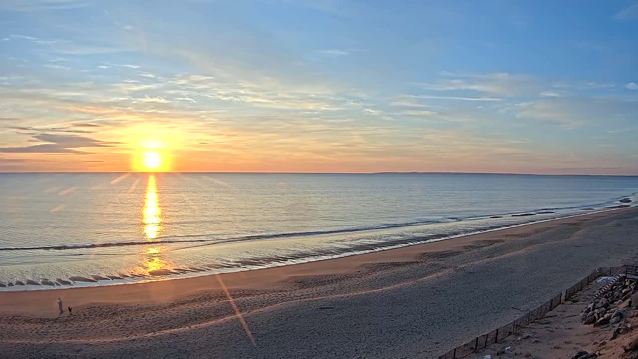 A sandy beach stretches out to meet a calm ocean under a vibrant sunrise.