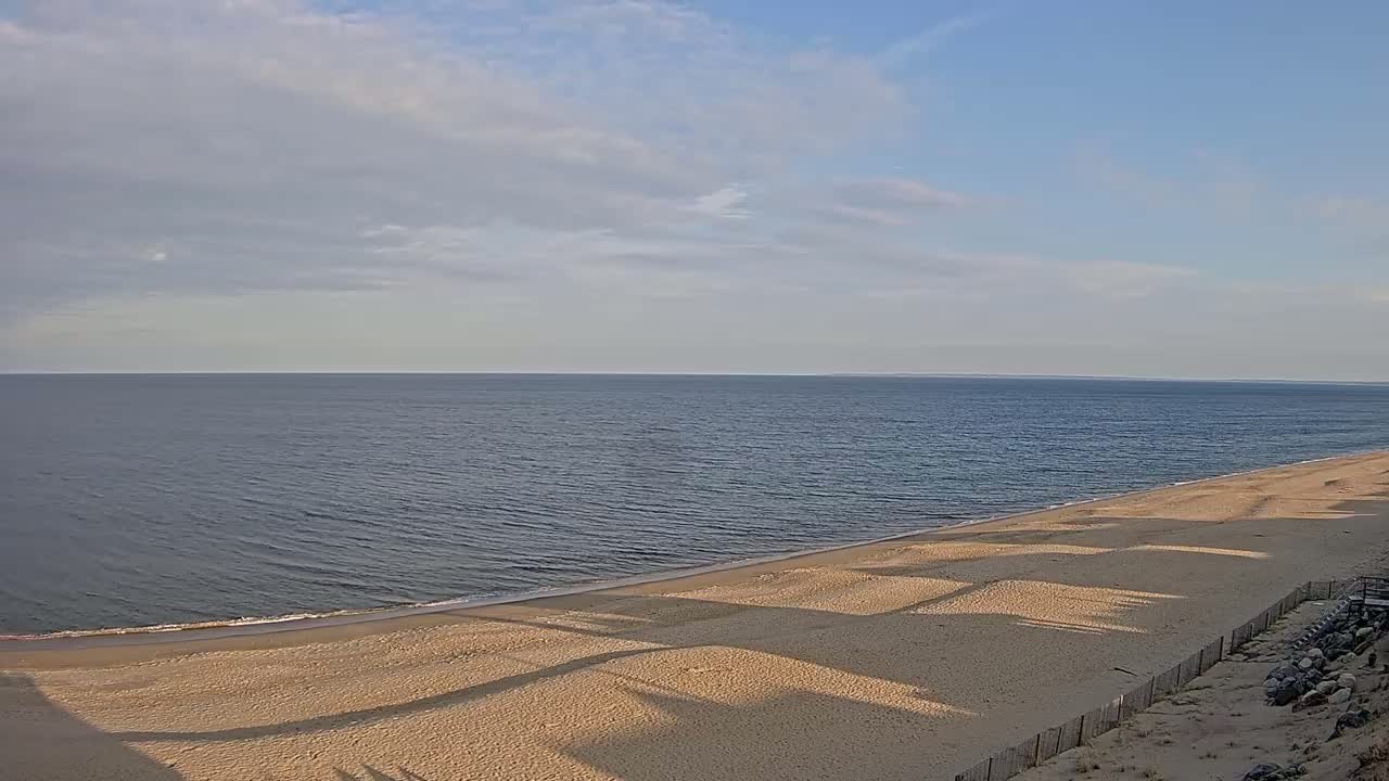 A sandy beach slopes down to a calm ocean under a mostly cloudy sky.