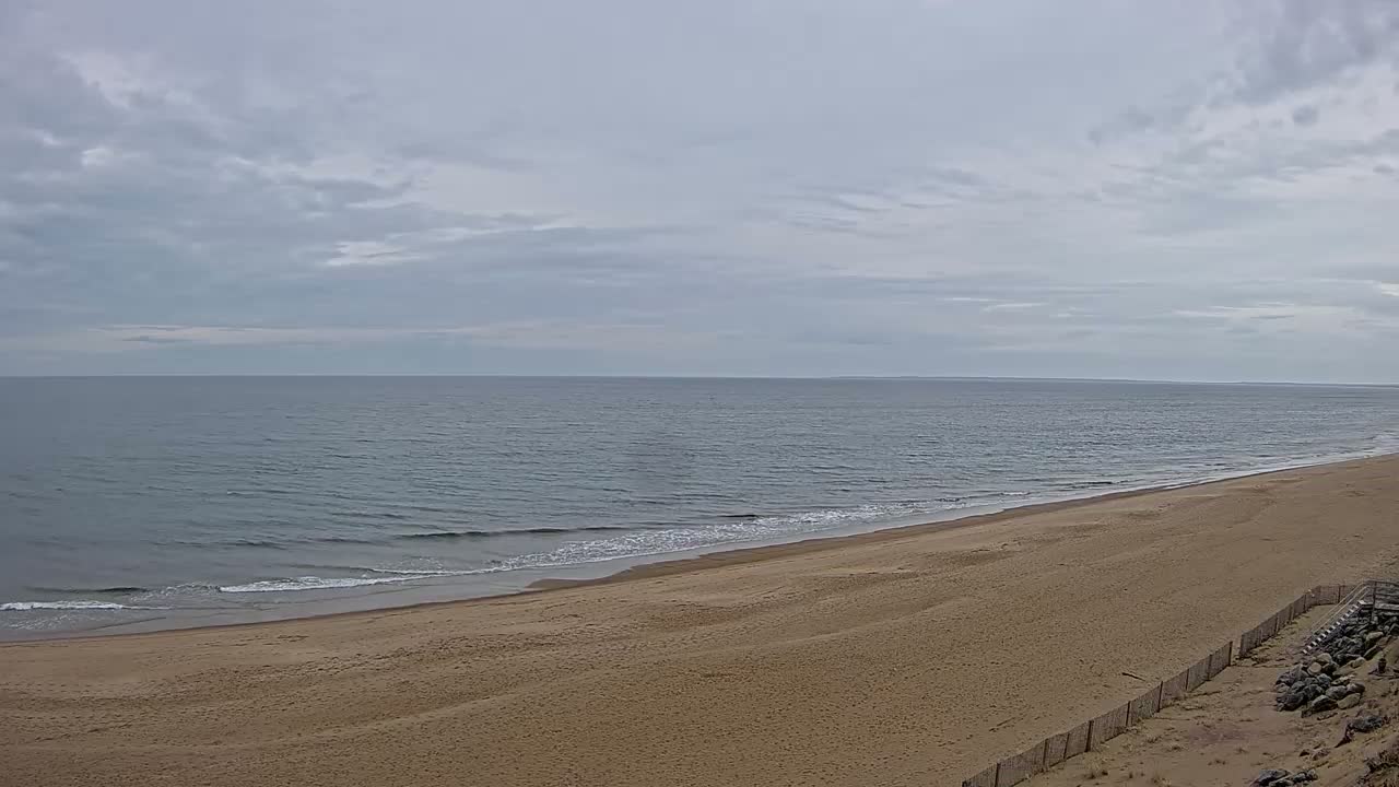 A long, sandy beach slopes down to a calm, gray ocean under a cloudy sky.