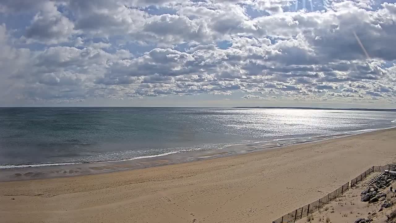 A wide sandy beach slopes gently down to a calm ocean under a partly cloudy sky.