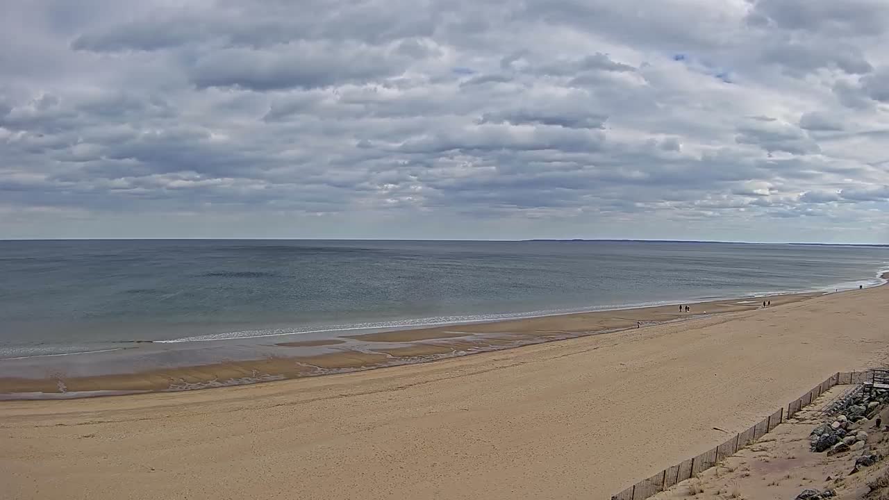A long, sandy beach stretches to a calm, gray-blue ocean under a cloudy sky.