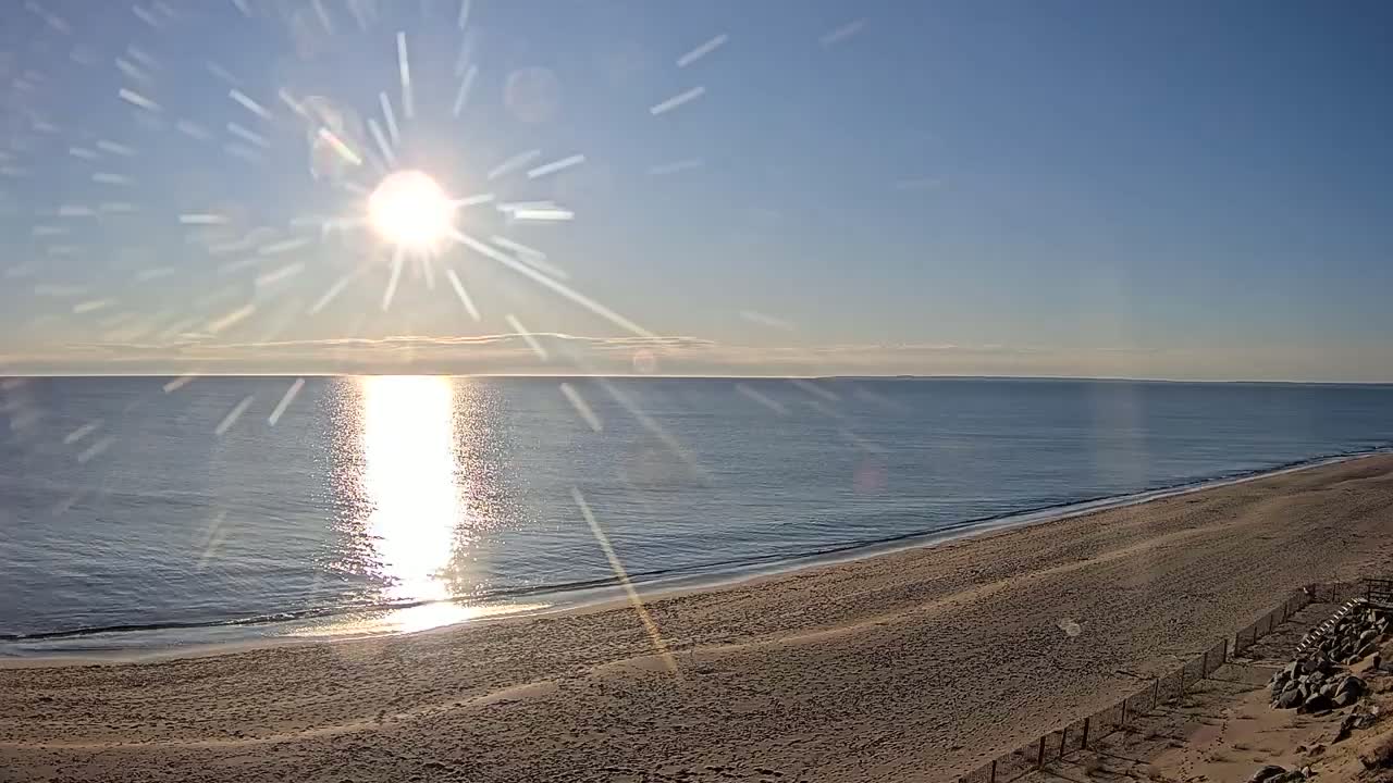 A sandy beach slopes down to a calm ocean reflecting the bright, sunlit sky.