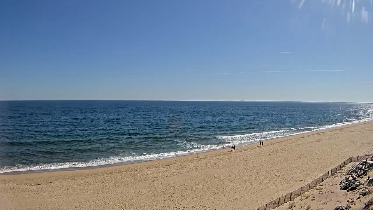 A sandy beach stretches along a calm ocean under a clear blue sky.