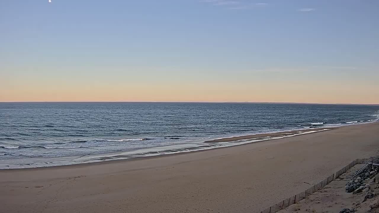 A sandy beach slopes gently down to a calm ocean under a pale, sunset sky.