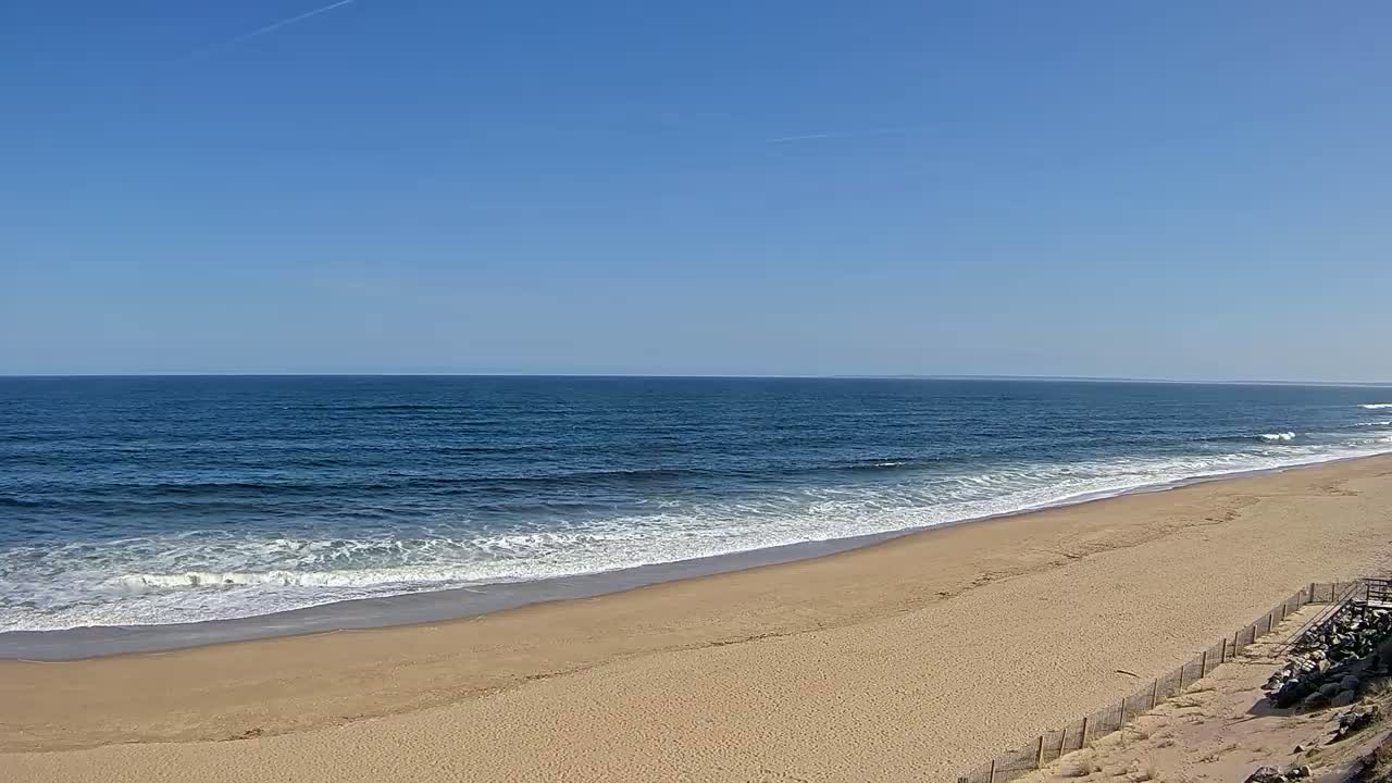 A sandy beach slopes down to a dark blue ocean with small waves under a clear blue sky.