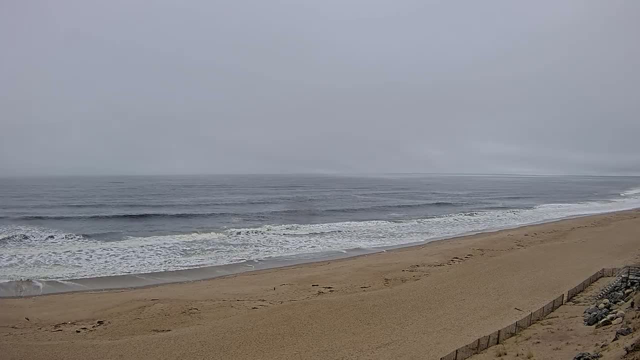 A wide sandy beach with moderate waves rolls onto the shore under a foggy sky.