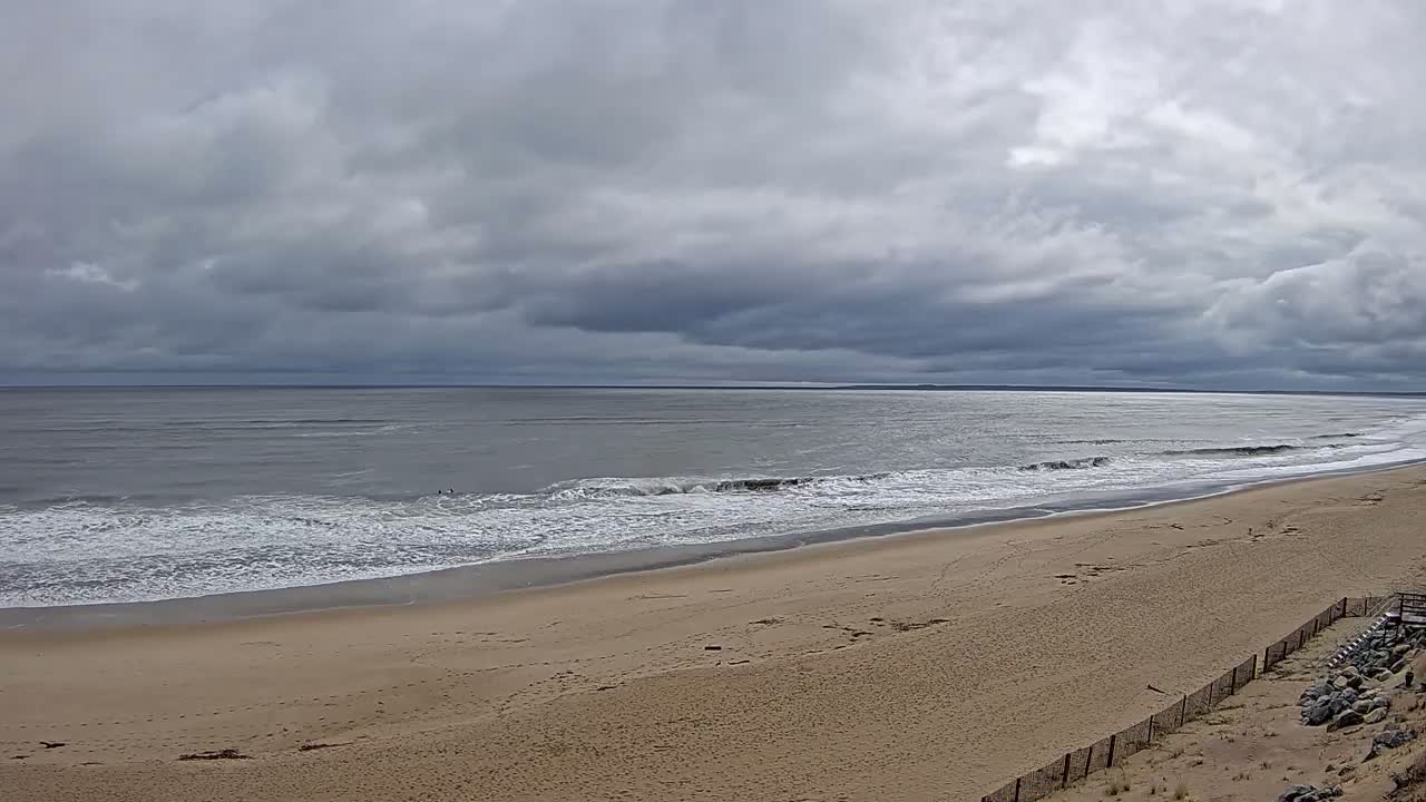 A wide, sandy beach slopes down to a gray ocean under a cloudy sky.