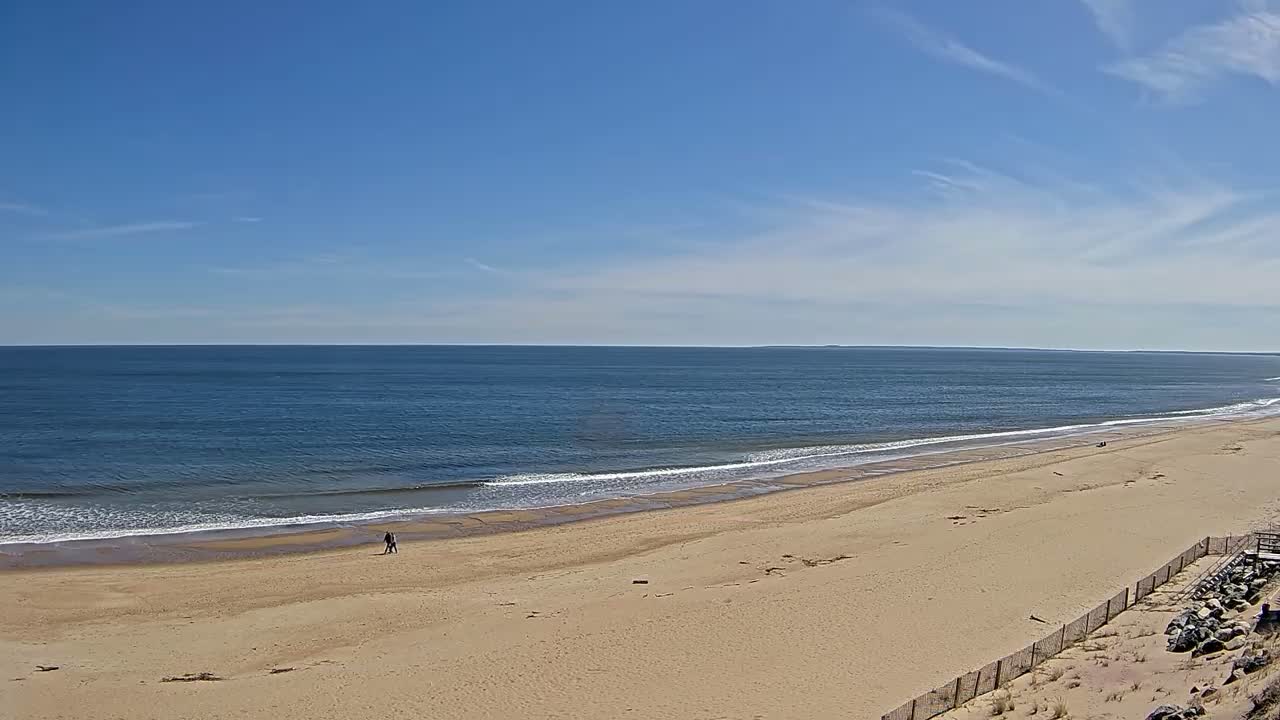 A wide sandy beach stretches to a calm ocean under a mostly clear blue sky.