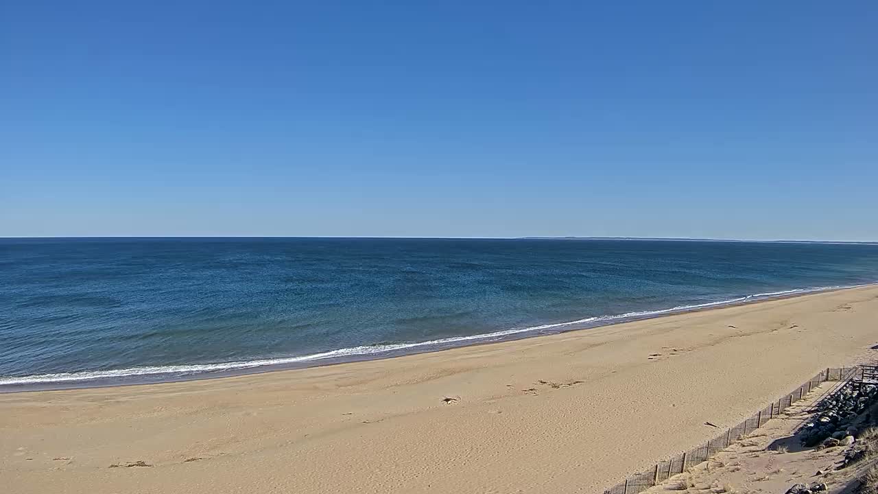 A wide sandy beach slopes gently down to a calm, blue ocean under a clear blue sky.
