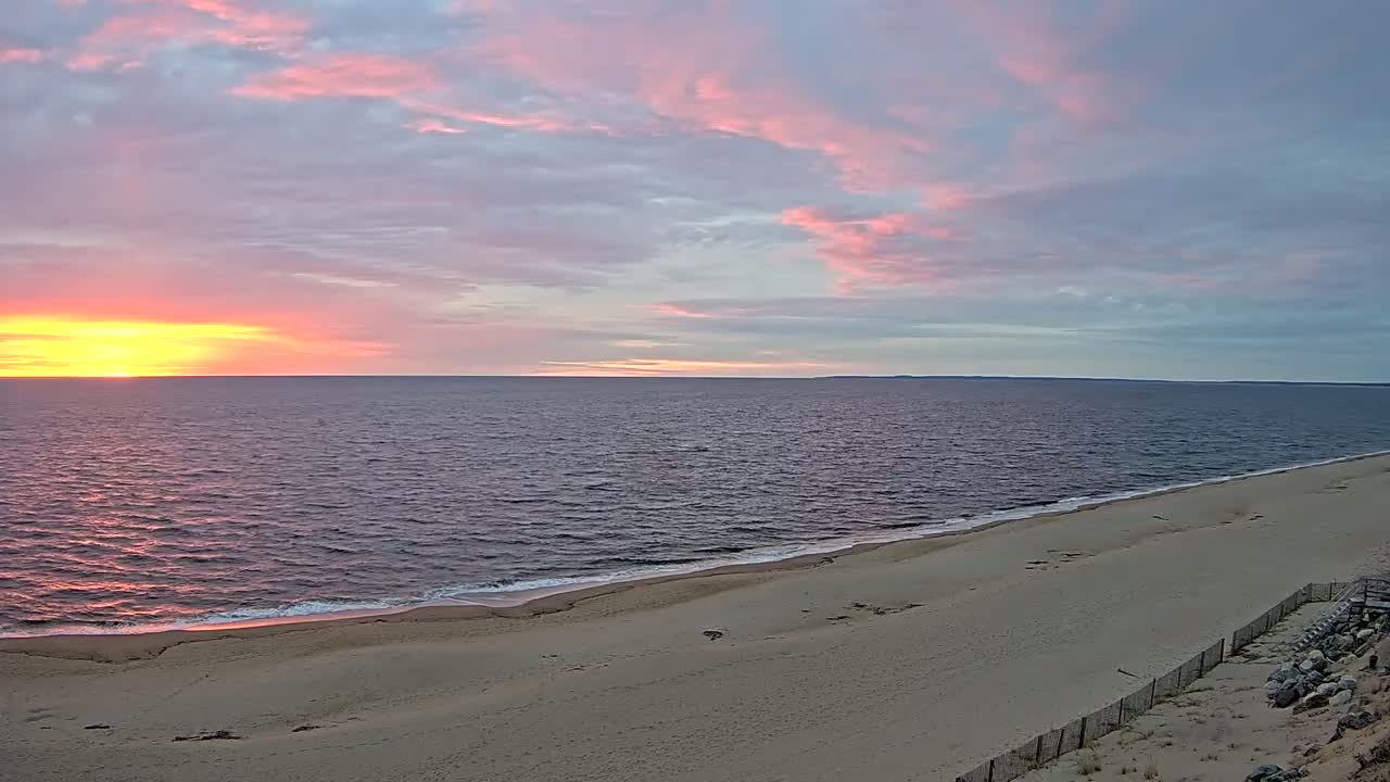 A sandy beach slopes down to a calm ocean under a pastel sunrise sky.