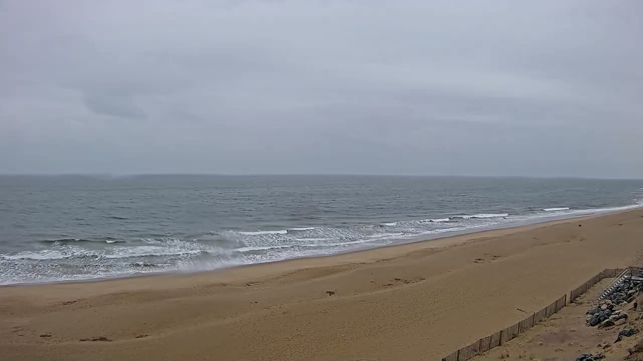 A wide sandy beach slopes down to a gray, wavy ocean under an overcast sky.
