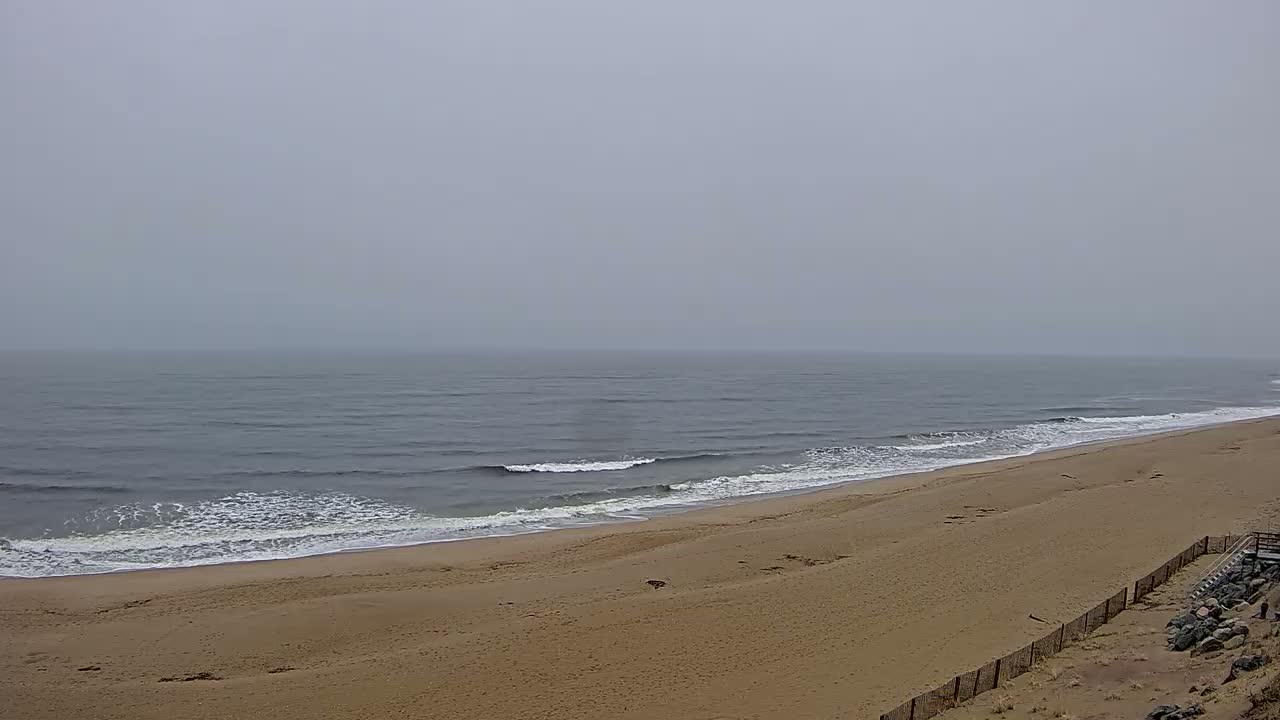 A wide sandy beach slopes gently down to a gray, somewhat choppy ocean under a foggy sky.