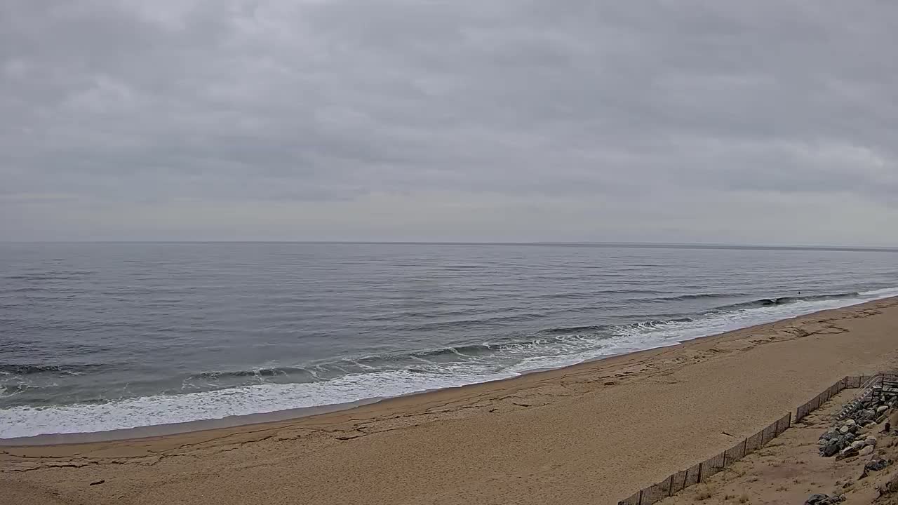 A long, sandy beach slopes down to a gray, wavy ocean under a cloudy sky.
