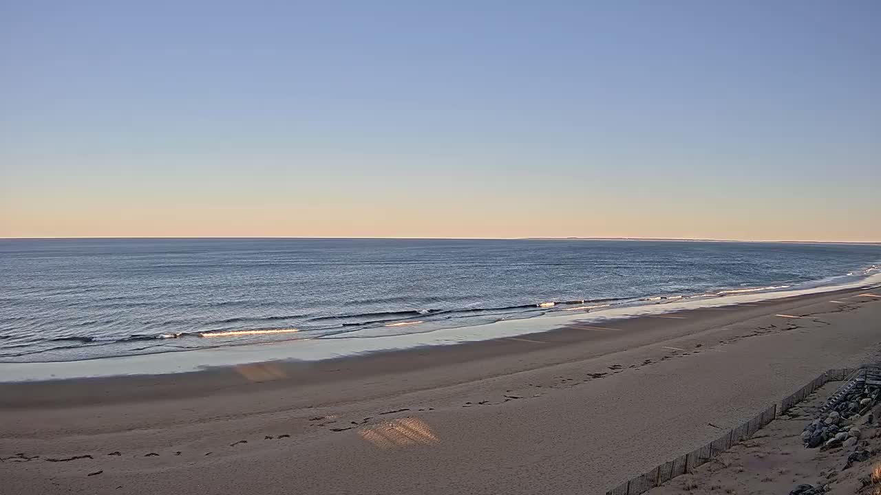 A sandy beach slopes down to a calm ocean under a clear, pale blue sky.