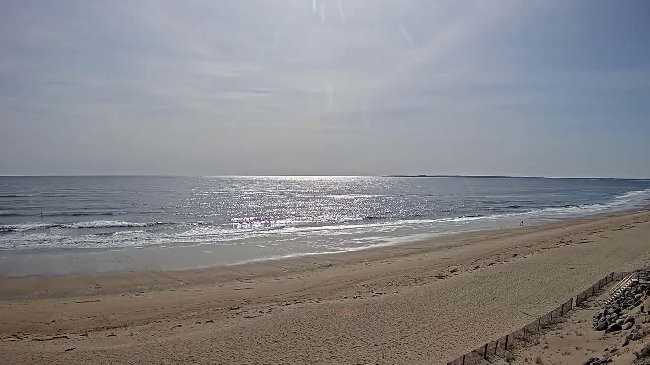 A wide sandy beach stretches to a calm, sunlit ocean under a mostly clear sky.
